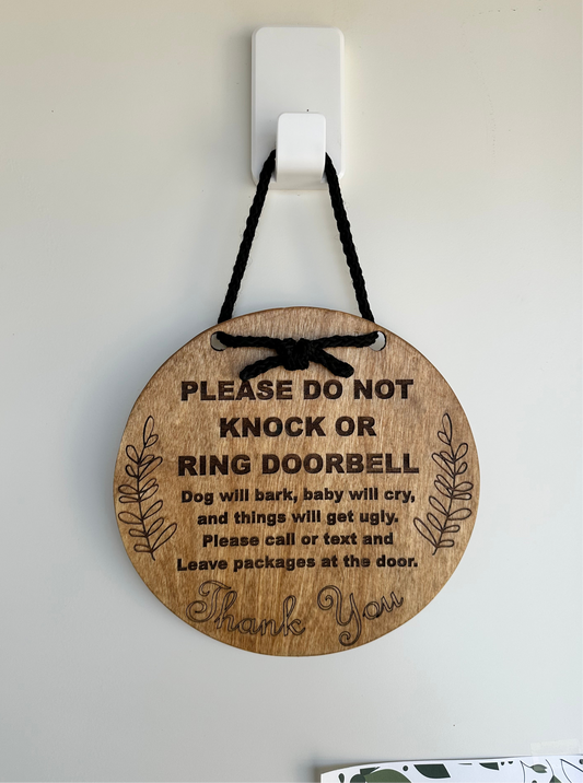 Circular wood front door sign that reads “please do not knock or ring doorbell. Dog will bark, baby will cry, and things will get ugly. Please call or text and leave packages at the door.”